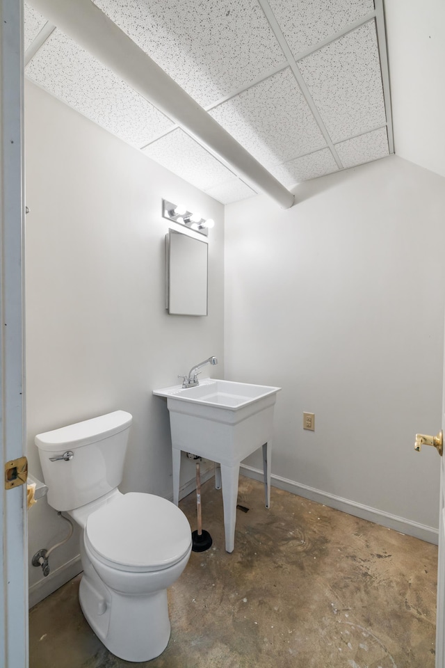 bathroom with concrete flooring, a drop ceiling, and toilet