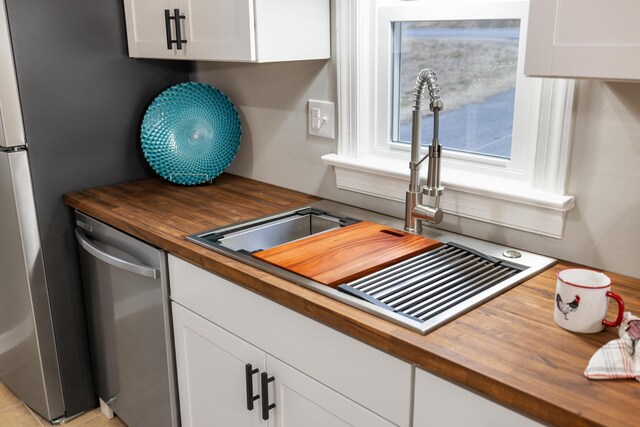 kitchen with stainless steel appliances, white cabinetry, butcher block counters, and sink