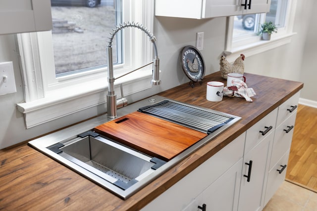 kitchen featuring butcher block counters, sink, light hardwood / wood-style flooring, and white cabinets