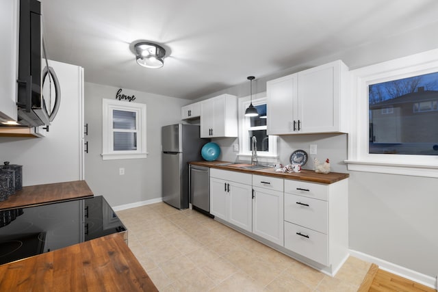 kitchen with butcher block counters, sink, white cabinetry, hanging light fixtures, and stainless steel appliances