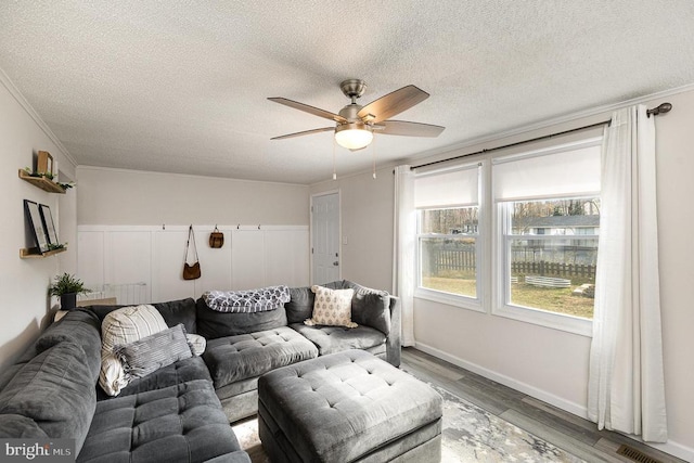 living room with wood finished floors, a ceiling fan, visible vents, ornamental molding, and a textured ceiling