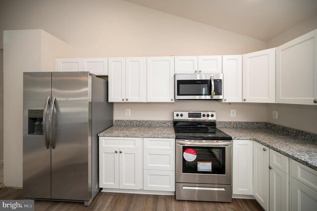 kitchen featuring stainless steel appliances, white cabinetry, vaulted ceiling, and light stone counters