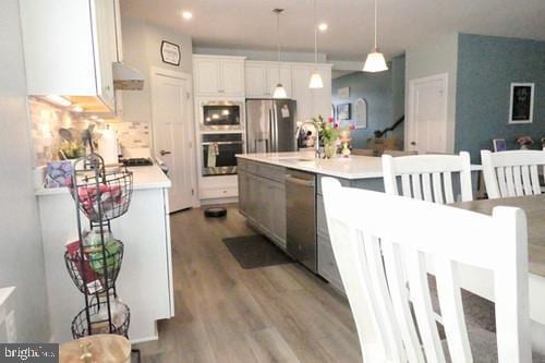 kitchen with appliances with stainless steel finishes, white cabinets, light countertops, and decorative light fixtures