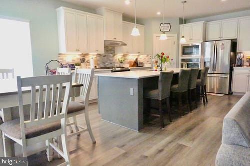 kitchen featuring white cabinetry, light countertops, appliances with stainless steel finishes, a center island, and decorative light fixtures