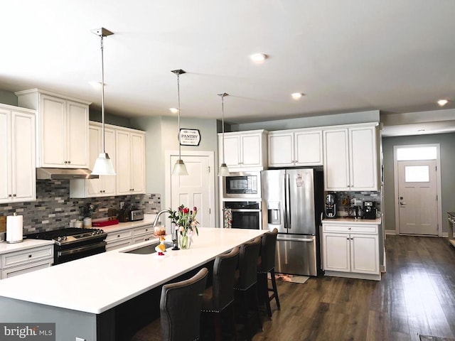 kitchen with under cabinet range hood, stainless steel appliances, a sink, light countertops, and decorative light fixtures