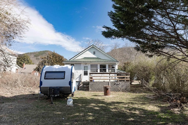 rear view of property with a deck with mountain view, metal roof, and a yard