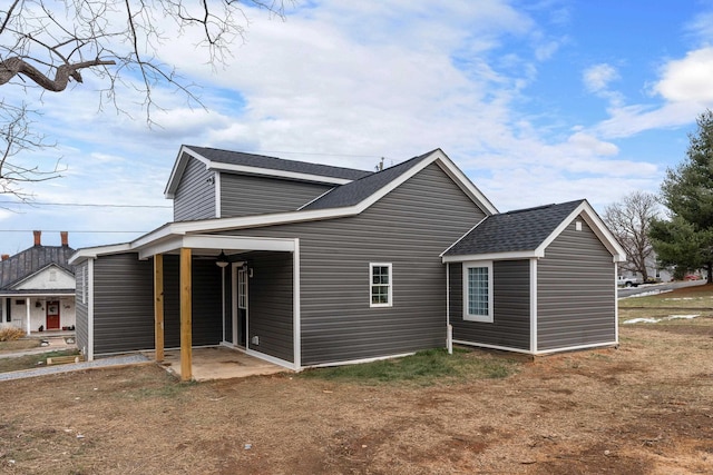 view of side of home featuring a patio and roof with shingles