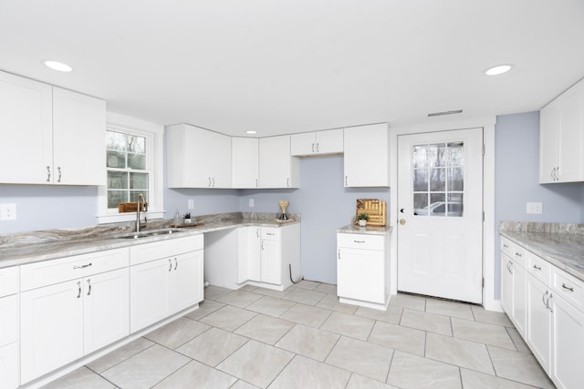 kitchen with light stone counters, recessed lighting, light tile patterned floors, white cabinets, and a sink