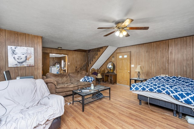 living area featuring wood finished floors, wood walls, a ceiling fan, and stairs