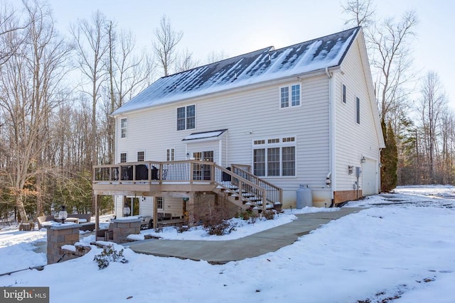 snow covered back of property featuring a garage and a deck