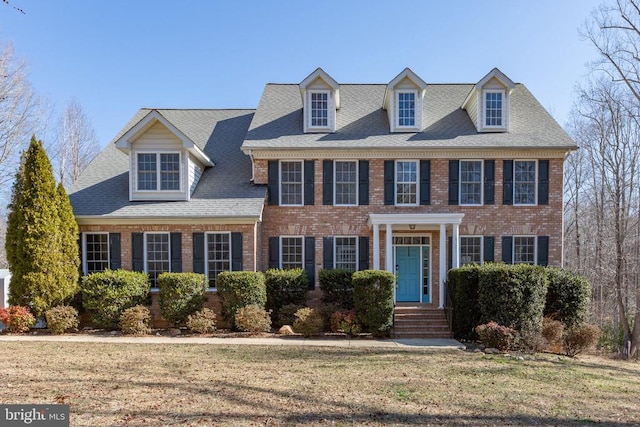 colonial-style house with roof with shingles, a front lawn, and brick siding