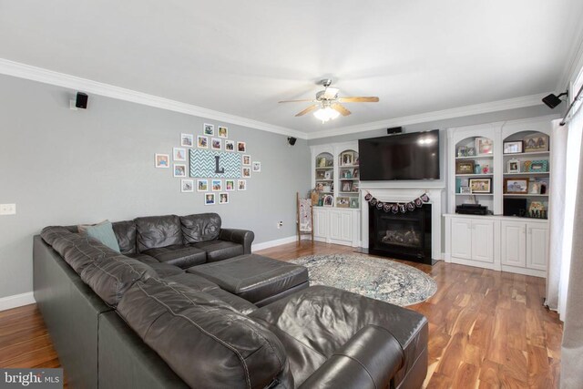 living room featuring ornamental molding, built in features, hardwood / wood-style flooring, ceiling fan, and a fireplace