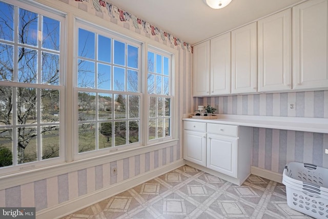 interior space featuring light floors, white cabinetry, wallpapered walls, and baseboards