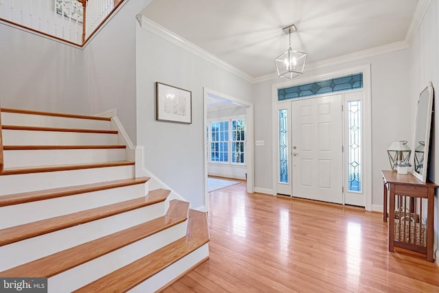 foyer entrance with crown molding, baseboards, stairs, light wood-style flooring, and an inviting chandelier