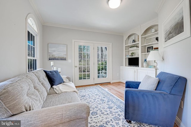 living room featuring built in shelves, wood finished floors, baseboards, and ornamental molding