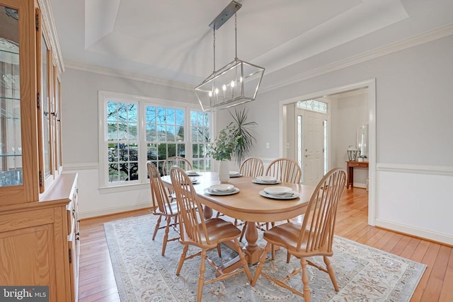 dining room with light wood-style flooring, a raised ceiling, and ornamental molding