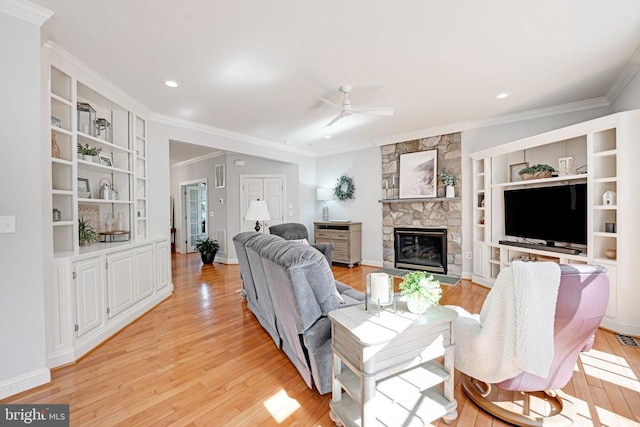 living area with a ceiling fan, baseboards, light wood finished floors, ornamental molding, and a stone fireplace