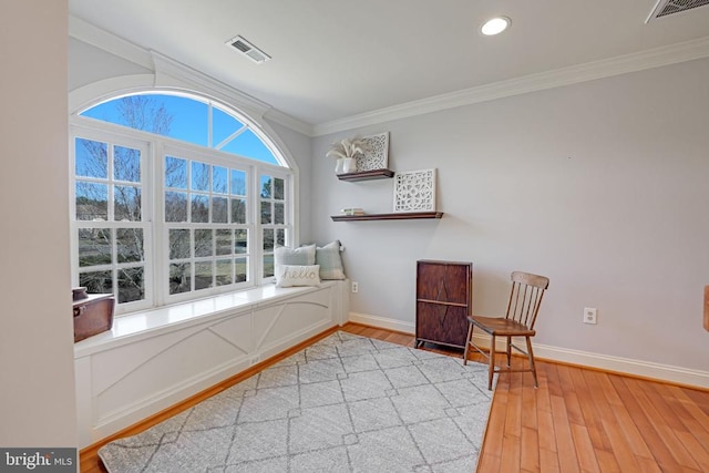 sitting room with baseboards, visible vents, light wood-type flooring, and ornamental molding