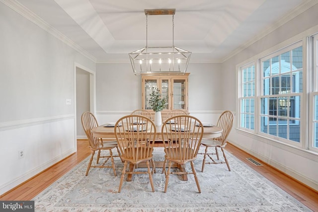 dining space featuring visible vents, a raised ceiling, baseboards, and wood finished floors