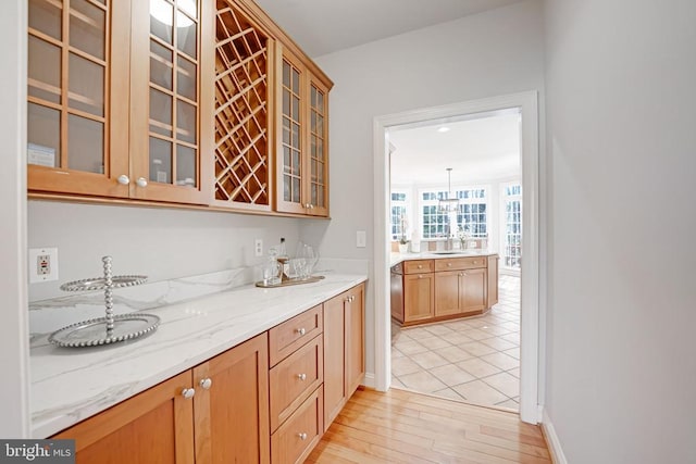 kitchen with light stone counters, baseboards, light wood finished floors, a sink, and glass insert cabinets