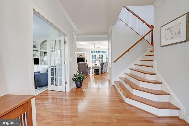 foyer entrance featuring a fireplace, ornamental molding, stairs, light wood-style floors, and french doors