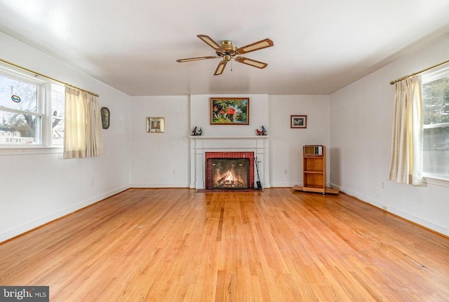 unfurnished living room with light wood-type flooring, a wealth of natural light, and a brick fireplace