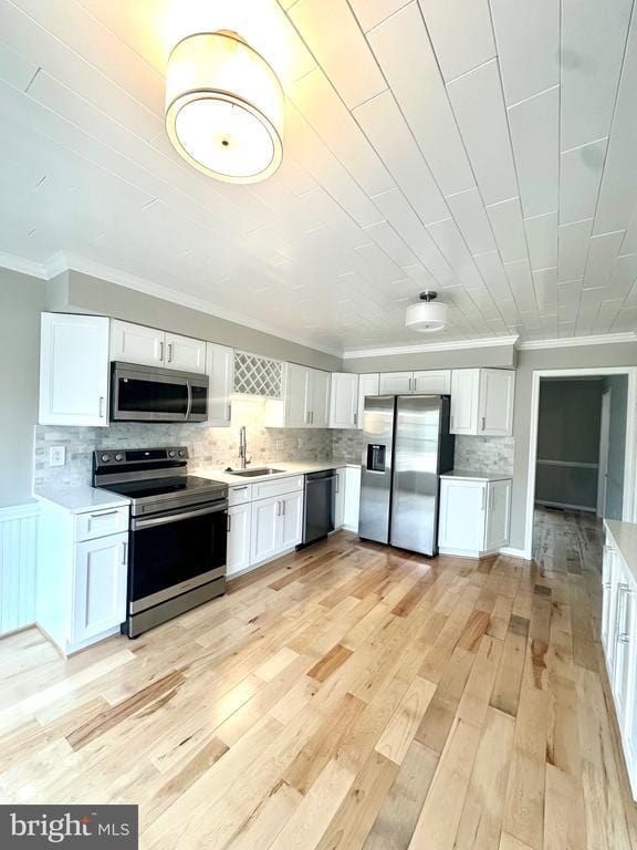kitchen with stainless steel appliances, light countertops, ornamental molding, light wood finished floors, and a sink