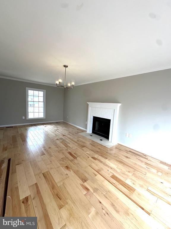 unfurnished living room with an inviting chandelier, light wood-style floors, baseboards, a fireplace with flush hearth, and crown molding