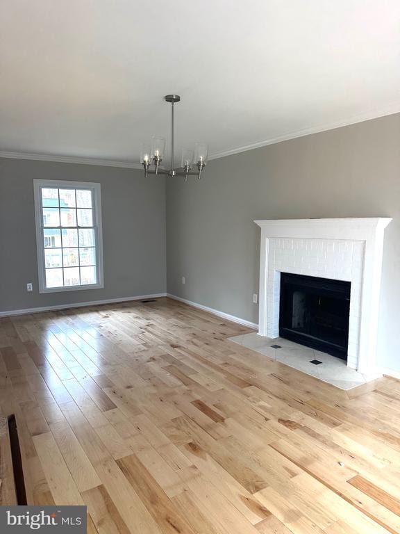 unfurnished living room featuring ornamental molding, a brick fireplace, baseboards, light wood-type flooring, and a notable chandelier