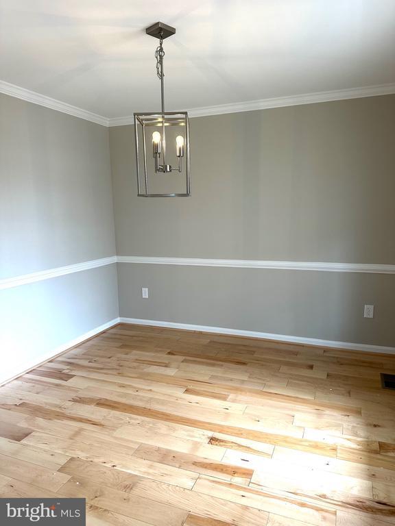unfurnished dining area featuring hardwood / wood-style floors, baseboards, a chandelier, and crown molding