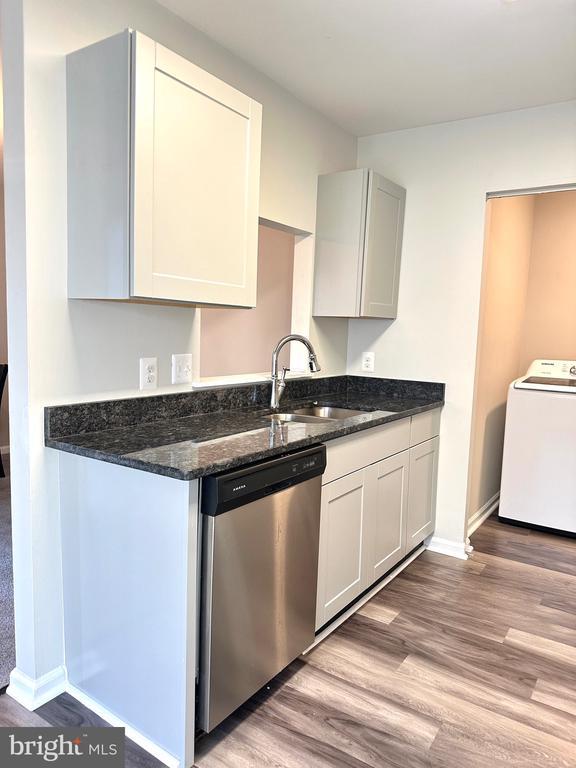 kitchen with sink, dishwasher, dark stone countertops, white cabinets, and washer / clothes dryer