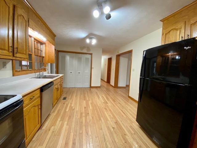 kitchen featuring sink, light hardwood / wood-style flooring, black refrigerator, range with electric stovetop, and stainless steel dishwasher