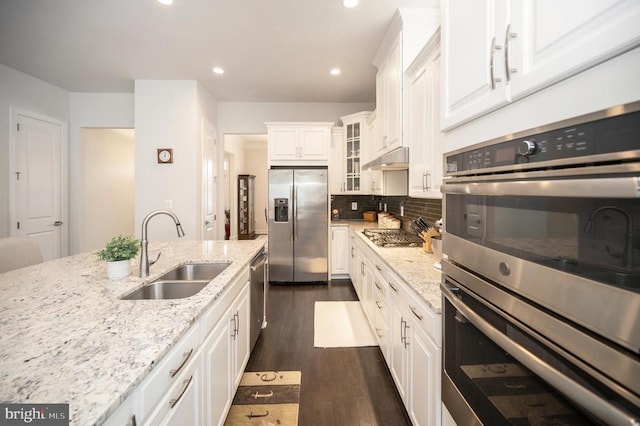 kitchen with stainless steel appliances, white cabinetry, light stone countertops, and sink