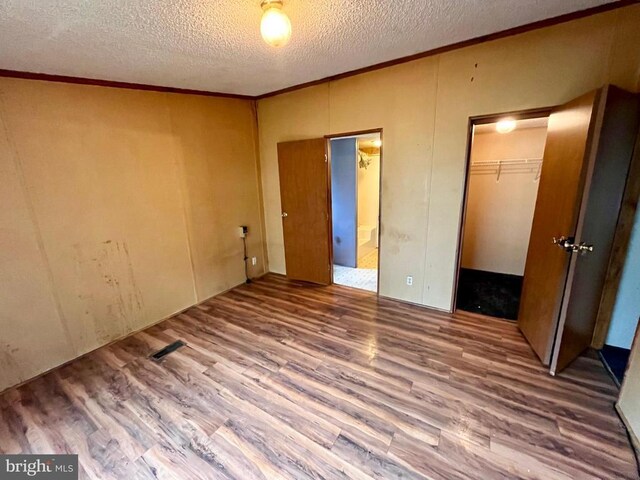 unfurnished bedroom featuring a walk in closet, a textured ceiling, crown molding, wood finished floors, and a closet