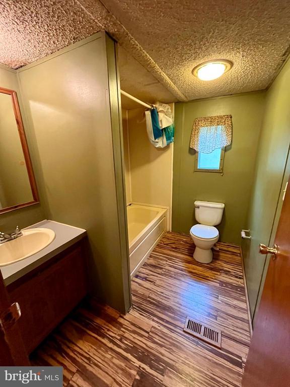full bath featuring visible vents, wood finished floors, toilet, a textured ceiling, and shower / washtub combination