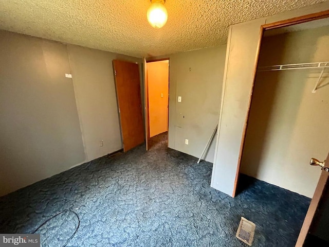 unfurnished bedroom with visible vents, a textured ceiling, a closet, and dark colored carpet