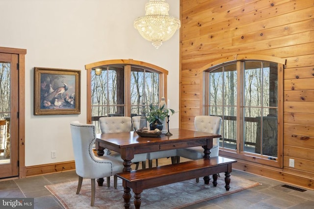 dining space with visible vents, wood walls, stone tile floors, and an inviting chandelier