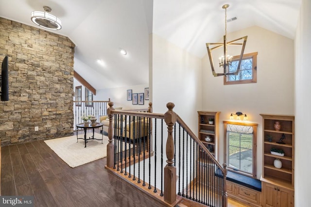 hall with a notable chandelier, wood finished floors, visible vents, an upstairs landing, and vaulted ceiling