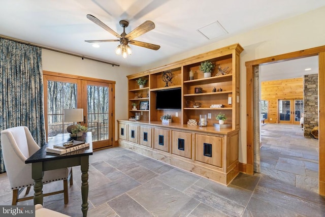 office with stone tile floors, wooden walls, ceiling fan, and french doors