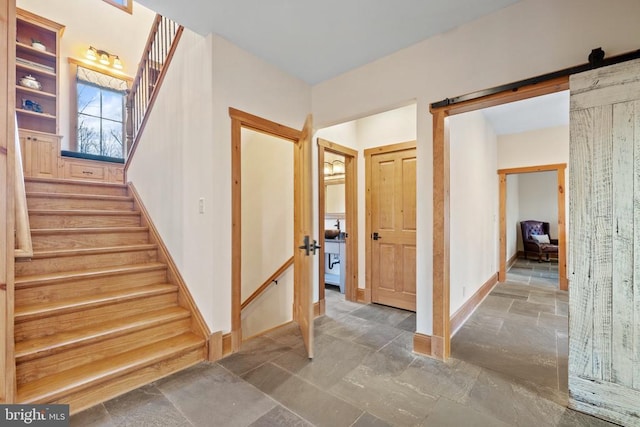 stairs with a barn door, baseboards, and stone tile flooring