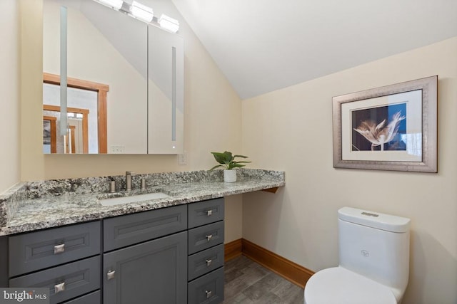 half bathroom featuring lofted ceiling, toilet, vanity, wood finished floors, and baseboards