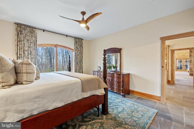 bedroom with a ceiling fan, baseboards, multiple windows, and stone tile floors