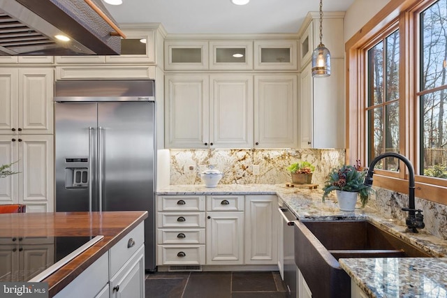 kitchen featuring range hood, pendant lighting, appliances with stainless steel finishes, glass insert cabinets, and a sink