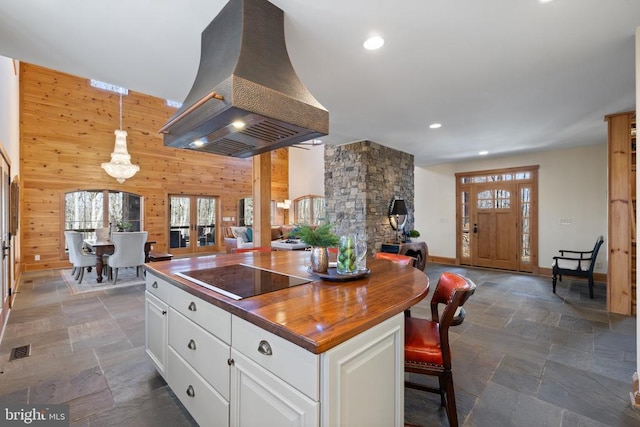 kitchen with black electric stovetop, wooden walls, stone tile floors, island range hood, and open floor plan