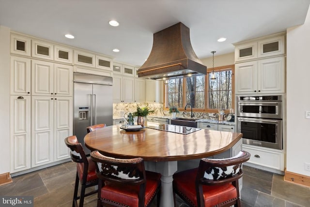 kitchen with stainless steel appliances, stone tile flooring, a sink, a kitchen island, and island range hood