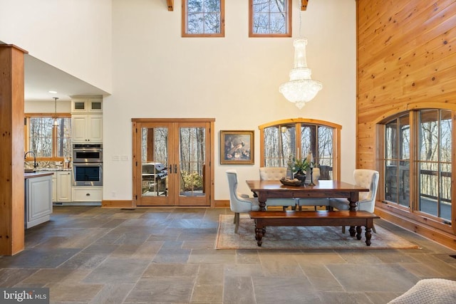 dining area with french doors, stone tile floors, wood walls, a chandelier, and baseboards