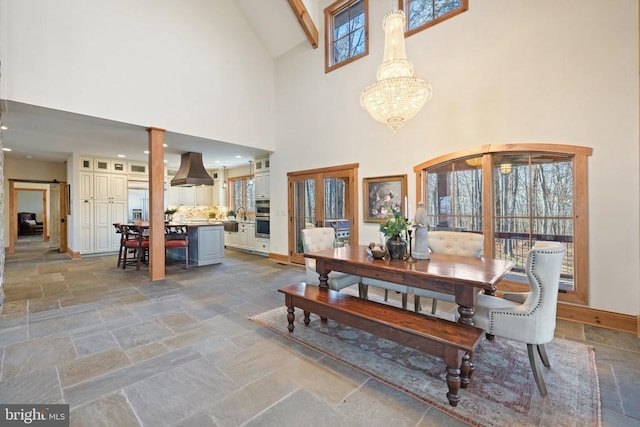 dining area featuring baseboards, a high ceiling, a chandelier, and stone tile flooring