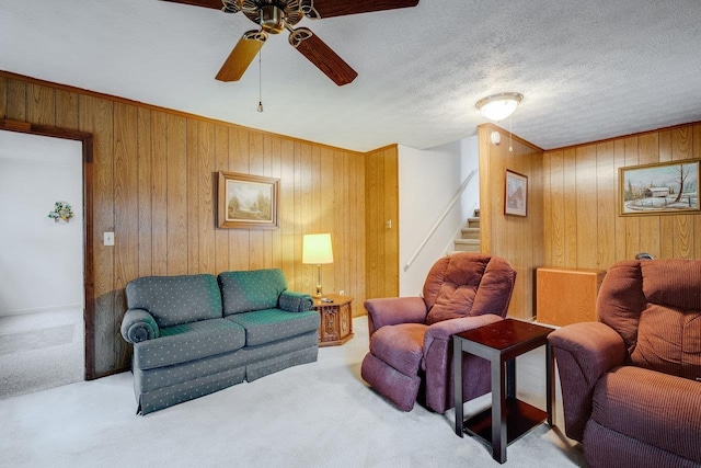 living room featuring ceiling fan, light carpet, a textured ceiling, and wood walls