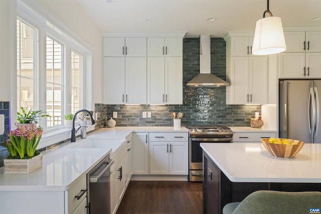 kitchen with dark wood-style flooring, wall chimney range hood, light countertops, a sink, and stainless steel appliances