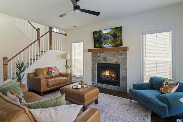 living area featuring stairs, wood finished floors, baseboards, a tiled fireplace, and a ceiling fan